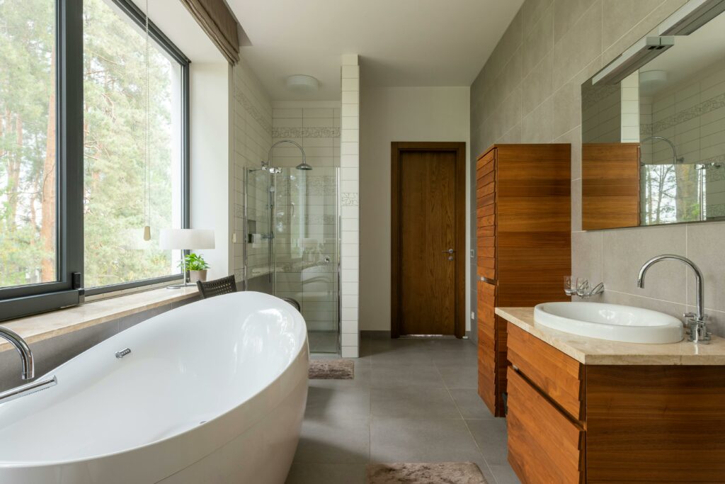 A modern bathroom features a freestanding bathtub, wooden cabinetry, a large window, a sink with a countertop, and a glass-enclosed shower.